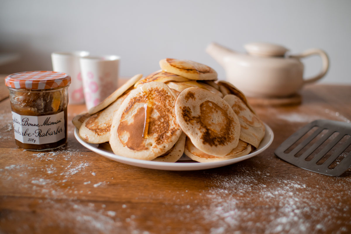 Vue réconfortante dune montagne de pancakes dégoûlinant de sirop dérable. Sur le côté se trouve un pot de confiture et une théière est en arrière-plan.