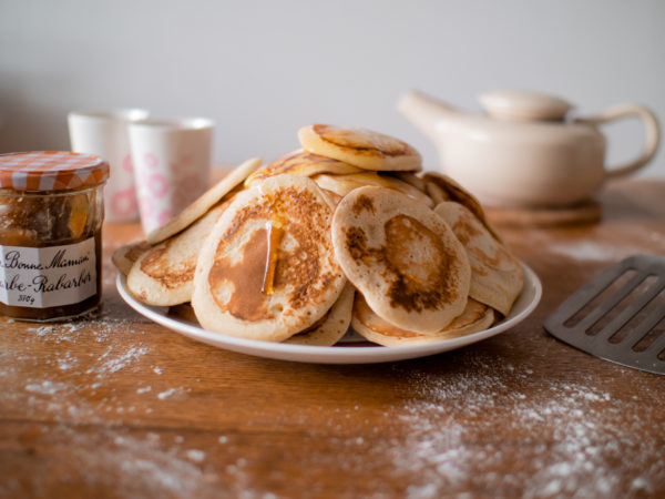 Vue réconfortante dune montagne de pancakes dégoûlinant de sirop dérable. Sur le côté se trouve un pot de confiture et une théière est en arrière-plan.