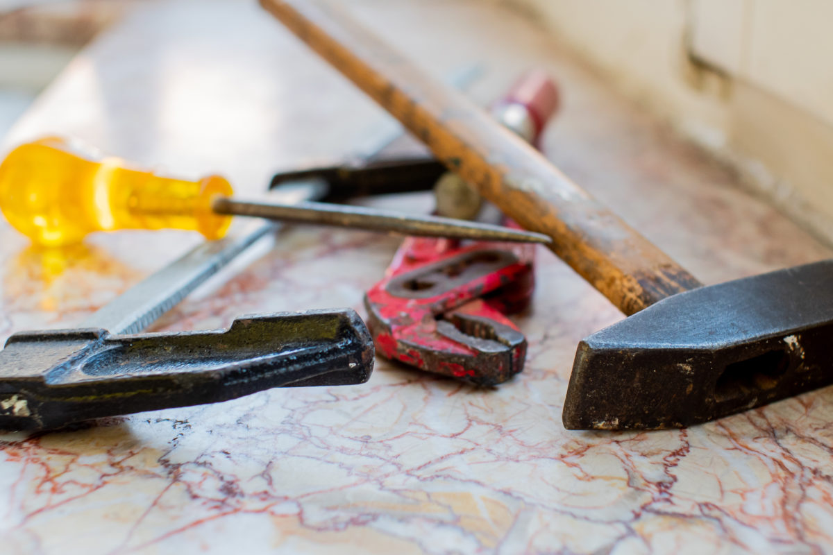 Des outils sont posés sur un plan en marbre. On y voit notamment tournevis, clef anglaise et marteau...