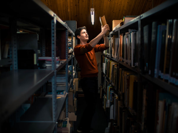 Un jeune homme; debout dans un des rayons du centre de documentation, tient dans ses mains un ouvrage. Son visage resplendit.
