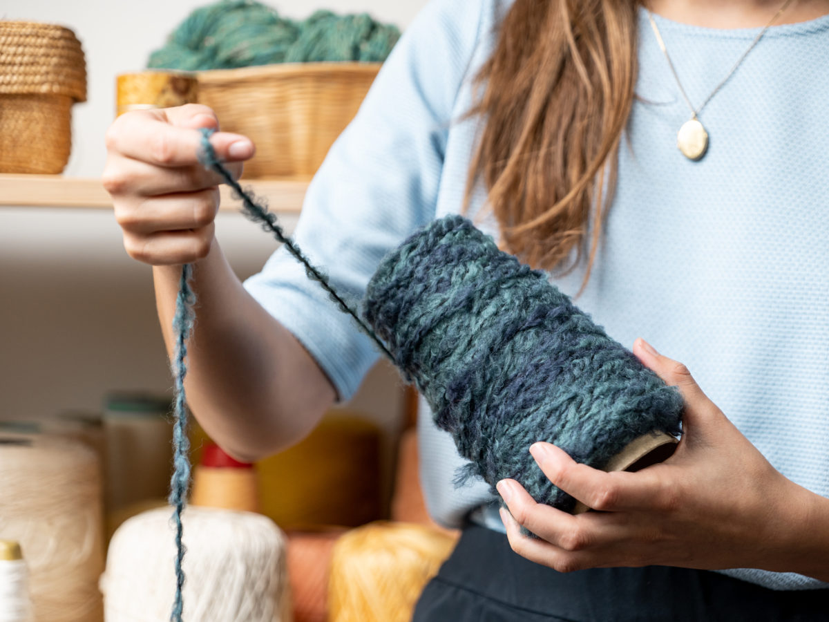 La designer textile Saskia déroule un fil de laine bleu-gris.