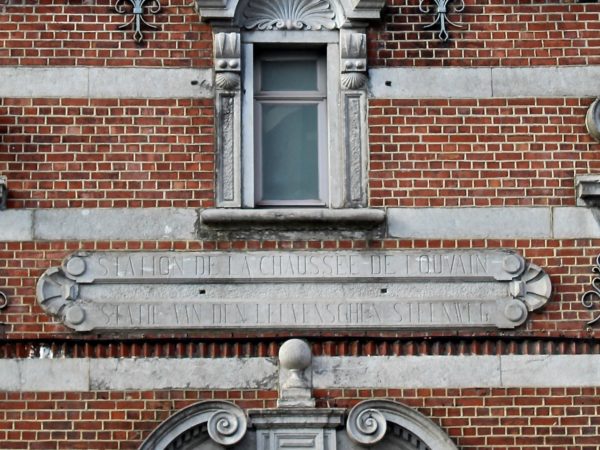 Cartouche en pierre sur une façade avec l'inscription "Station de la chaussée de Louvain"